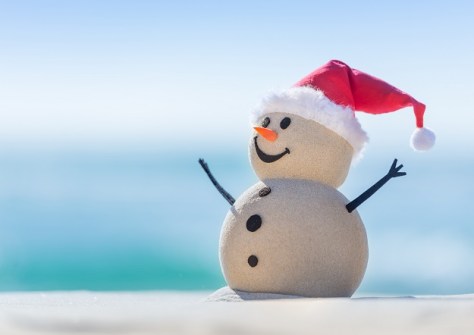 A snowman made of sand on a beach, wearing a Santa hat