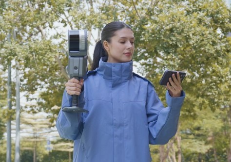 A woman holding a laser scanning unit in one hand and a smartphone in the other
