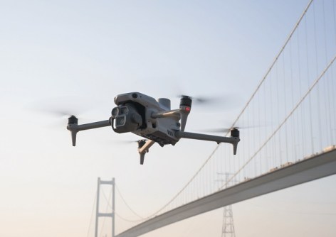 One of the range of DJI drones flying in front of a bridge
