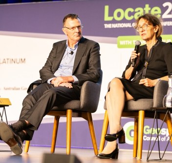 Two people seated on a stage at a conference, one with a microphone in her hand