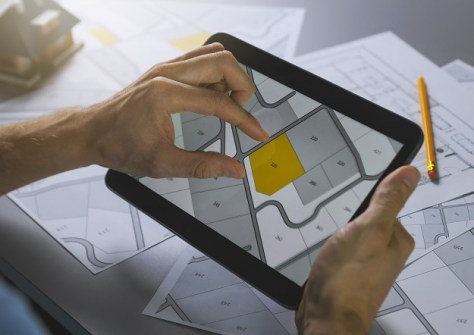 A pair of hands holding an iPad, on which is displayed a map of houses such as would be produced as CAD files.