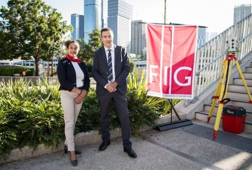 Diane Dumashie and Steve Jacoby standing next to a low wall with plants, at the unveiling of the commemorative permanent survey mark in Brisbane.
