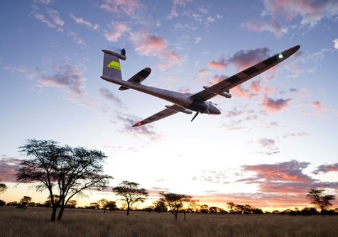 Seen from below, a QS Trinity Pro long-range VTOL mapping drone flying low over the ground, doing reality capture from the air