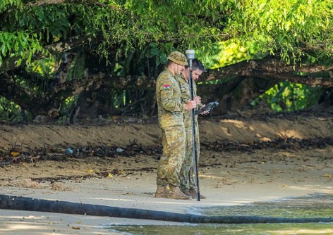 Two men in army clothes standing on a beach in the Solomon Islands, using surveying equipment