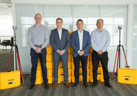 Four men standing in a row, alongside two Trimble R980 GNSS receivers