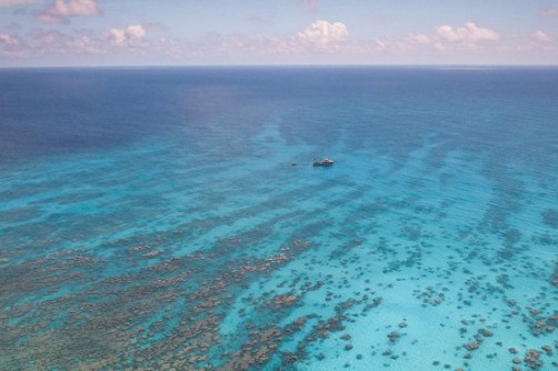 An aerial view of a small ship and boat in shallow water with reefs below, in Kiribati