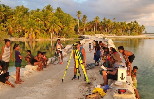 A man using surveying equipment while children look on, in Kiribati