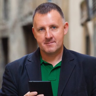 Head and shoulders image of Ed Parsons, looking at the camera while holding a mobile phone