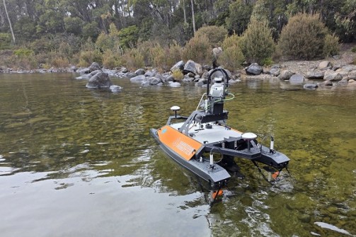A small catamaran floating on water near the shore of Lake St Clair, equipped with instruments for mapping the lakebed and shoreline