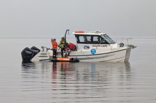 A small boat with three people, floating in fog on the waters of Lake St Claire