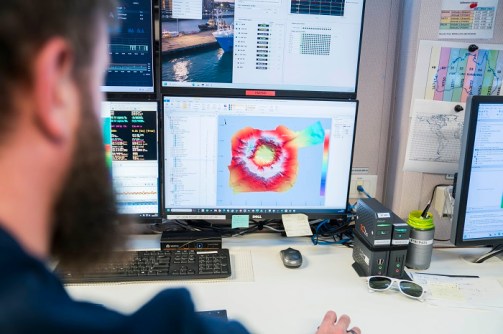 A view over the shoulder of a bearded man, who is looking at a computer screen showing the Hunga Volcano seafloor map
