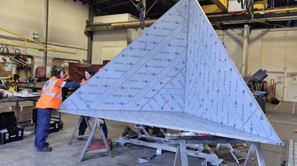 Two people wording with a large trihedral corner reflector, used to reflect radar waves from satellites