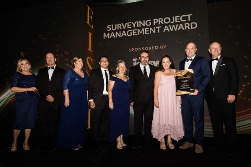 Nine people standing together at the EISSI awards ceremony, with one of them holding the award