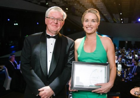 A man and a woman standing next to each other, with the woman holding an award
