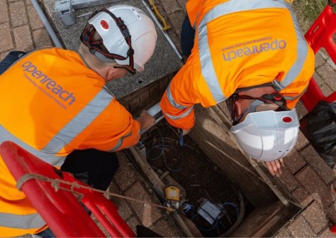 A photo taken from overhead, of two men in hardhats and fluoro vests, working on underground pipes and cables.