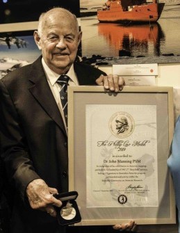 A man in a suit holding a framed certificate and medal in its snap case. The man is John Manning, who has been awarded in the Australia Day honours list.