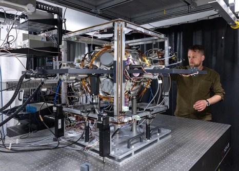 A man in a laboratory testing one of Imperial College's quantum sensors, which looks like a metal sphere held within a metal box frame, with lots of wires going in and out.