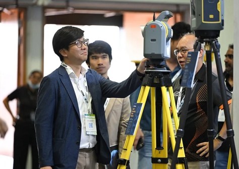 Three men look at a piece of surveying equipment at the Geo Connect Asia conference