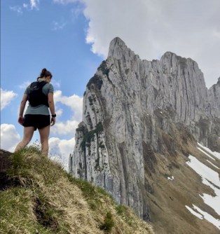Phoebe Davis walking in Swiss mountains, with high peaks in the background