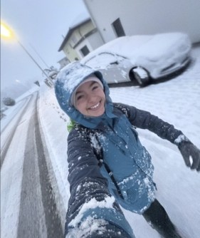 A selfie of Phoebe Davis walking along a snow-covered street with snow falling