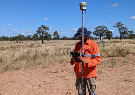 Sijan Bhandari, one of Australia's young professionals in surveying, standing in a clearing in a grassy field on a sunny day, holding a surveying pole and computer unit