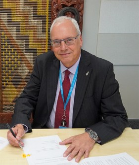 Adam Greenland, the new director of the International Hydrographic Organisation, posing at a desk with papers in front of him and a pen in his right hand