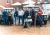 Nine men standing in front of cars in 1986, with GPS equipment on the ground in front of them