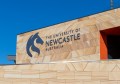 The University of Newcastle logo seen on a sandstone building exterior on a sunny day