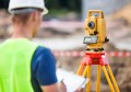 A surveyor holding a clipboard and looking at a surveying instrument atop a tripod
