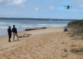 Two people standing on a beach, watch as a drone conducts a beach survey