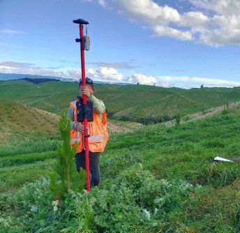 A person standing on a green grass-covered hill, using a surveying instrument fitted with a SouthPAN receiver for an accuracy boost