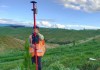 A person standing on a green grass-covered hill, using a surveying instrument fitted with a SouthPAN receiver