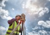 A surveyor looking through a surveying instrument, seen from below