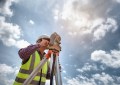 A surveyor looking through a surveying instrument, seen from below