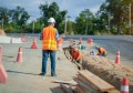 A man in hi-vis clothing supervising excavation activities at the side of a road.