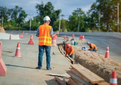 A man in hi-vis clothing supervising excavation activities at the side of a road.