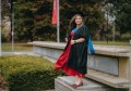 A GIS student standing wearing graduation robes