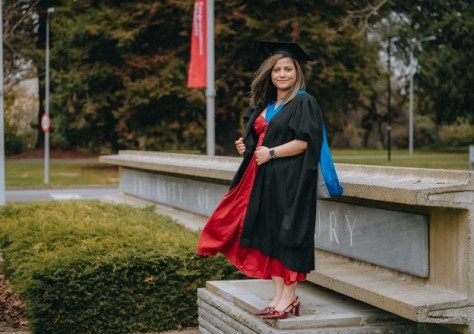 A GIS graduate standing wearing graduation robes