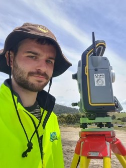 Bursary recipient, Connor Fox, standing next to a total station