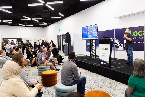 A man on a podium, speaking to an audience at the Locate conference