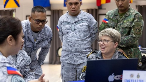 Royal Australian Navy Captain Fiona Ewington sitting at a desk, surrounded by five Philippine Navy personnel