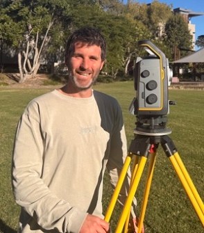 Bursary recipient, Rhys Alexander, standing next to a total station