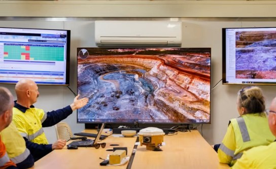 Four people seated at a desk in an office, looking at a computer screen on which is displayed an open cut mine