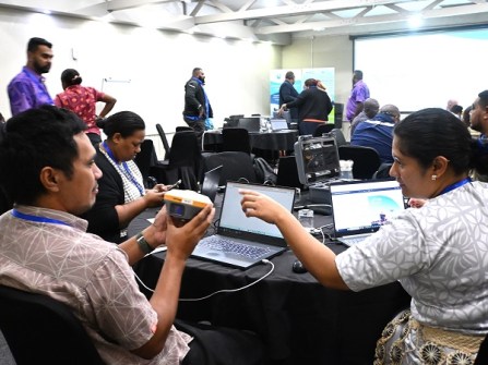People seated at round tables in a room, holding GNSS equipment and looking at laptop screens