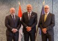 Three men, directors of the International Hydrographic Organization, pose for a photo indoors in front on flags