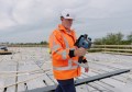 A man walking on a large roof, holding a LiDAR scanner