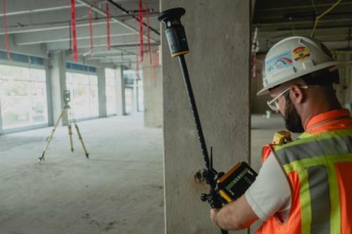 A man in a fluorescent safety jacket, holding a Trimble ST30 smart target