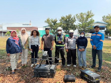 Eight people posing for a photo outside, with an environmental monitoring drone on the ground in front of them