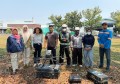 Eight people posing for a photo outside, with an environmental monitoring drone on the ground in front of them